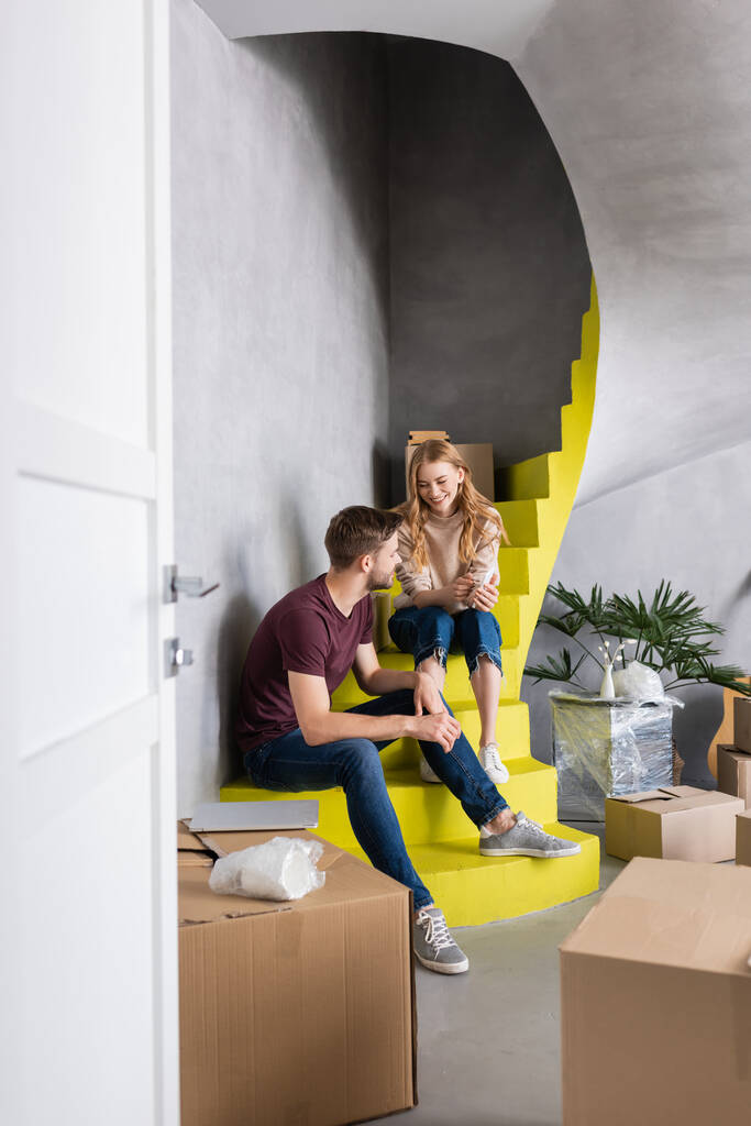 ボックスの近くの階段に座っている若い夫婦の選択的な焦点,移転の概念  - 写真・画像