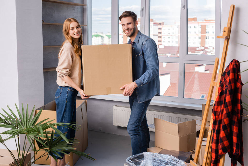 man en vrouw met kartonnen doos in de buurt van plant, bewegend concept - Foto, afbeelding