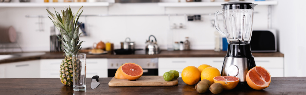 Panoramic shot of fresh fruits near blender on table in kitchen  - Photo, Image