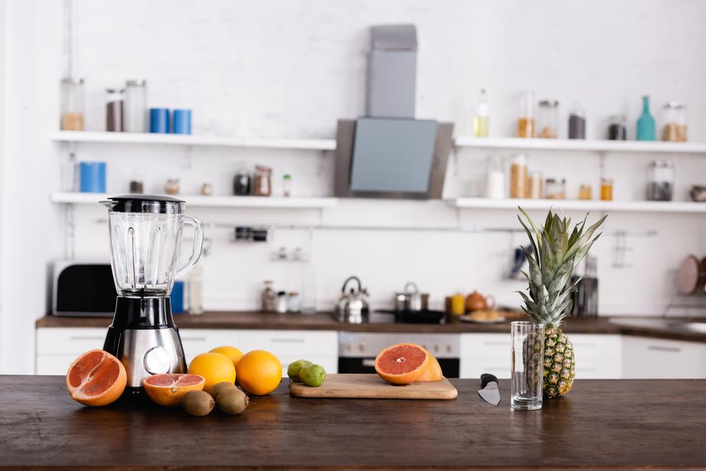 Свіжі фрукти на обробній дошці біля скла та блендера на кухонному столі
  - Фото, зображення