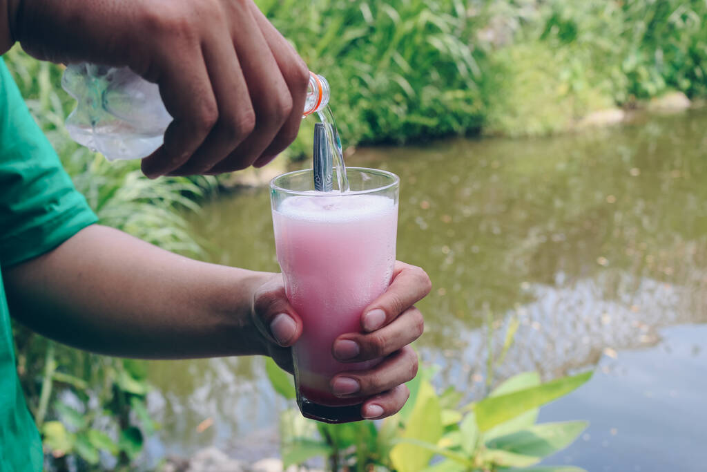 Чоловік наливає соду в склянку молока і червоного сиропу, щоб зробити рожеву молочну соду або Soda Gembira. - Фото, зображення