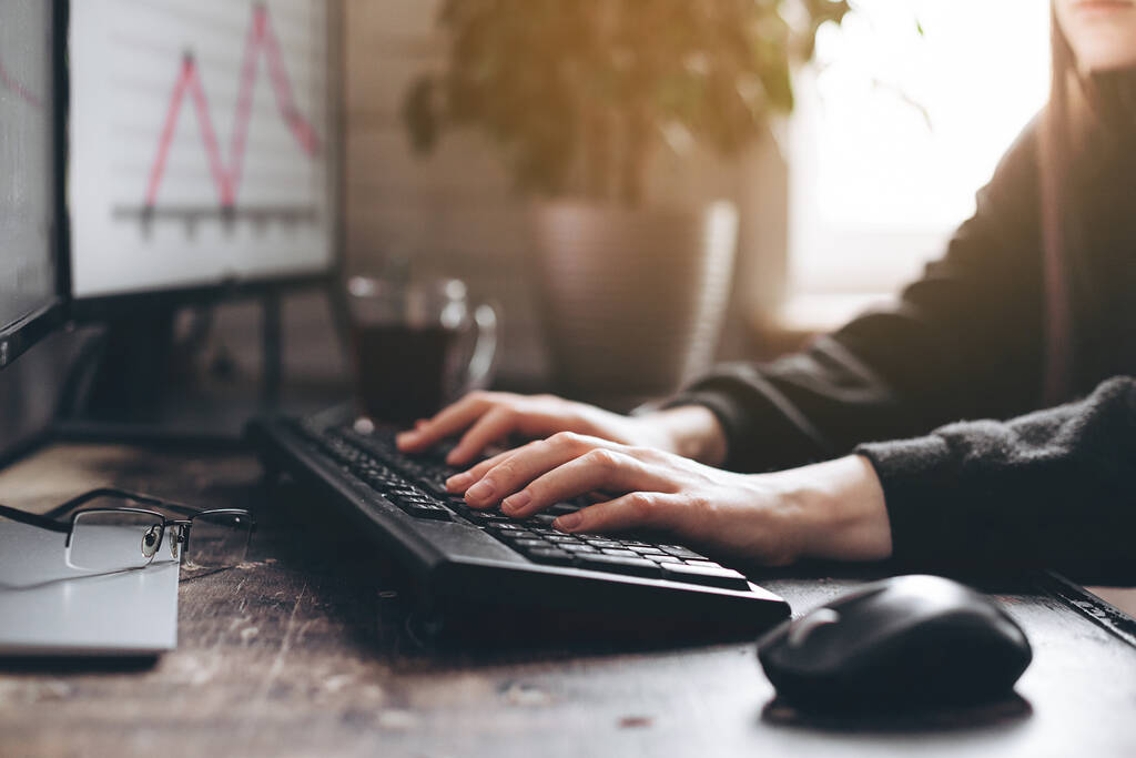 Žena pracující v domácí kanceláři ruku na klávesnici zblízka. Na pozadí monitorů klávesnice s grafem na slunci - Fotografie, Obrázek