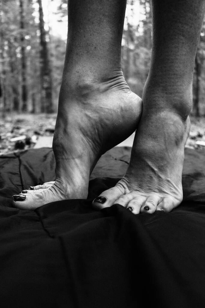 Gambe femminili, mani. bei piedi e palme su uno sfondo nero, primo piano. Fotografia in bianco e nero, luce naturale. - Foto, immagini