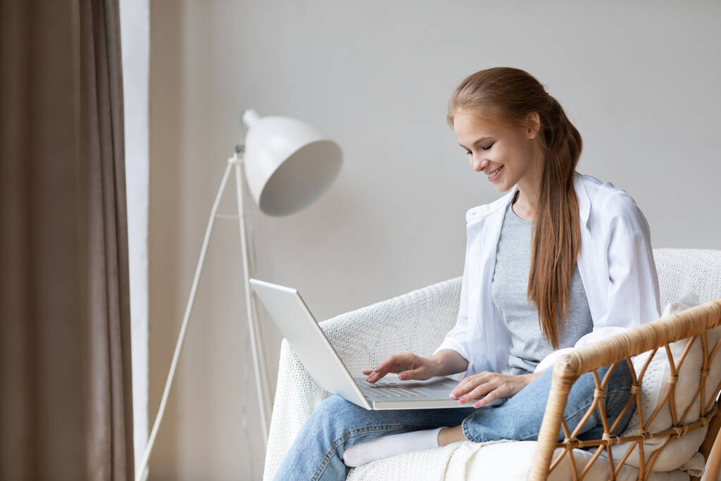 Freelancer mulher usando laptop enquanto sentado na cadeira confortavelmente em casa. Trabalho remoto ou estudo. - Foto, Imagem