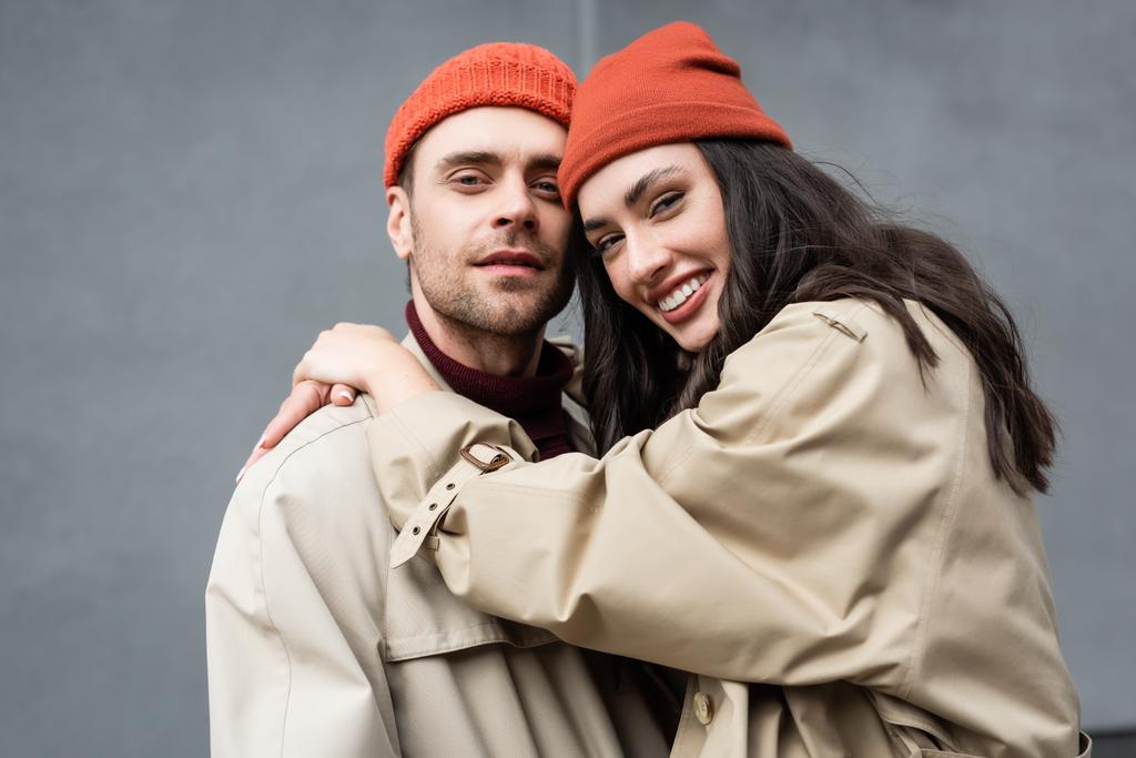trendy woman in beanie hat hugging man in trench coat  - Photo, Image