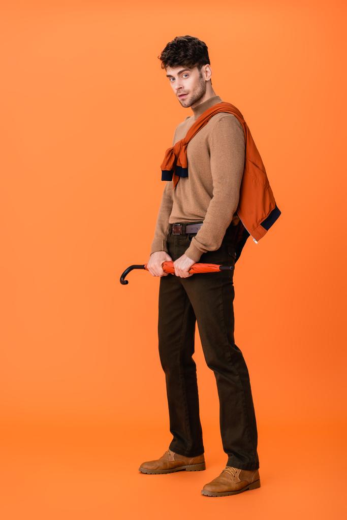 オレンジ色の傘を持っている秋の衣装の流行の男の完全な長さ  - 写真・画像