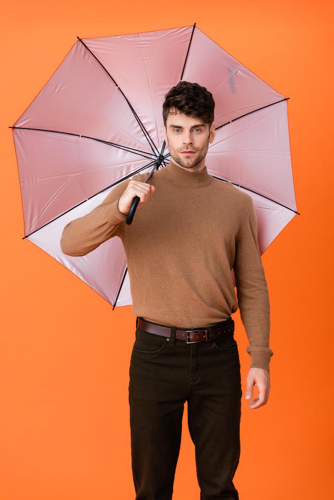 стильный мужчина в осеннем наряде стоит под зонтиком на апельсине  - Фото, изображение