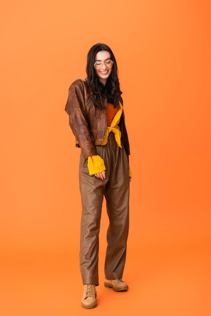 longitud completa de la mujer joven en traje de otoño y gafas de pie en naranja  - Foto, Imagen