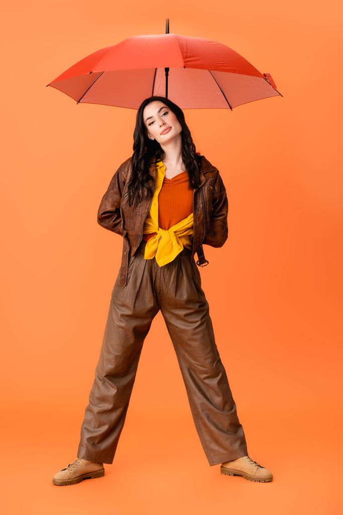 Sonbahar kıyafetleri ve botlarıyla turuncu üzerinde şemsiyesi olan genç ve şık bir kadın. - Fotoğraf, Görsel