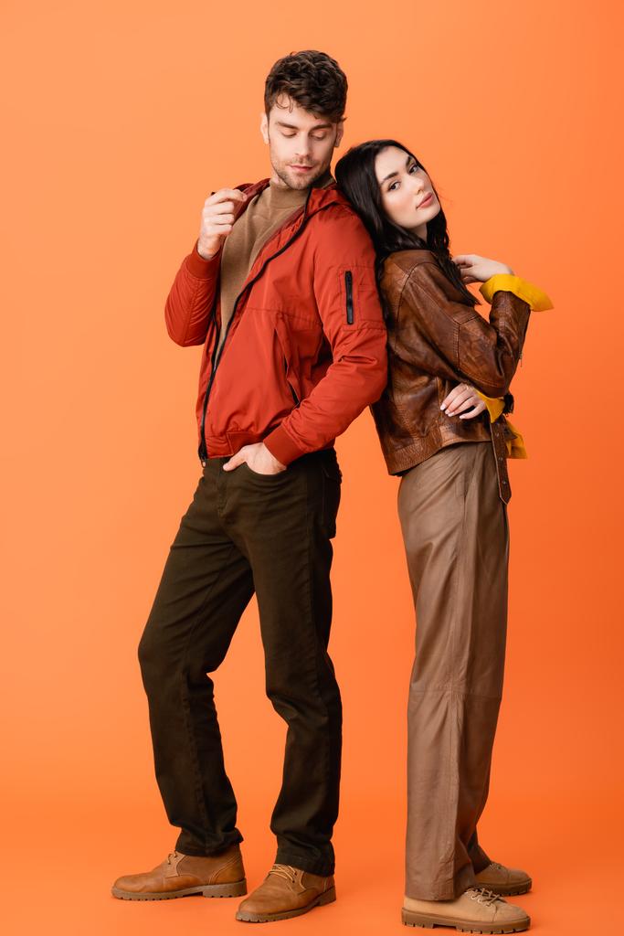 full length of trendy couple in leather jackets posing on orange - Photo, Image