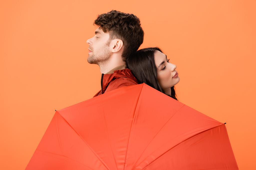 modieuze man en vrouw bij paraplu geïsoleerd op oranje - Foto, afbeelding