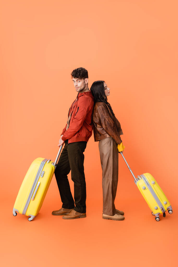 オレンジ色の黄色の荷物を背負ったまま立ち上がる秋の衣装を着たスタイリッシュなカップルの完全な長さ  - 写真・画像