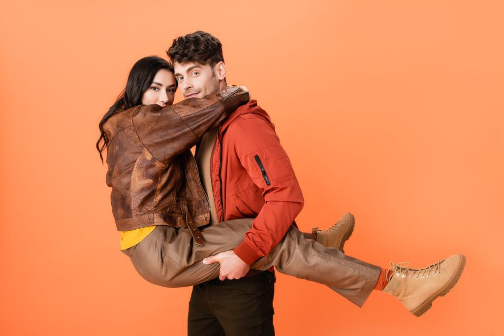 Trendiger Mann hält Frau im Herbst-Outfit auf Orange in den Armen  - Foto, Bild