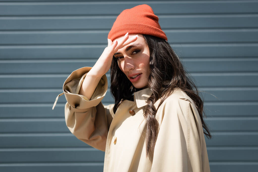 μελαχρινή γυναίκα σε καπέλο beanie κρύβεται από τη λιακάδα με το χέρι - Φωτογραφία, εικόνα