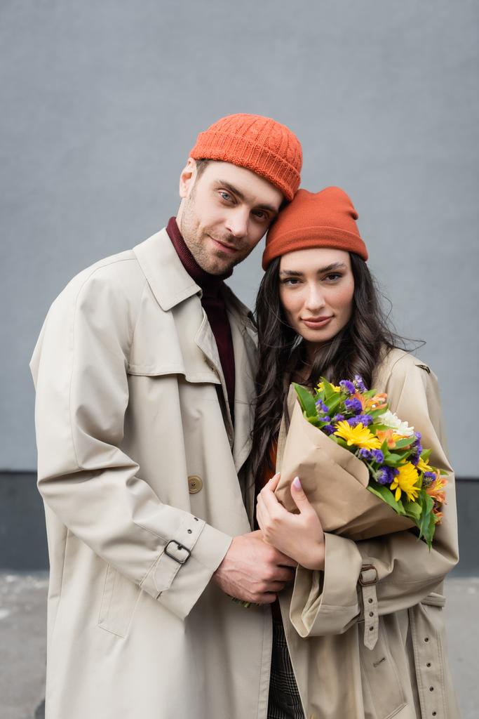 couple élégant en trench manteaux et chapeaux tenant bouquet de fleurs  - Photo, image