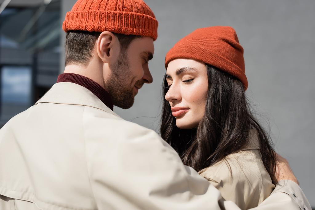pareja de moda con los ojos cerrados en abrigos de trinchera y sombreros - Foto, Imagen