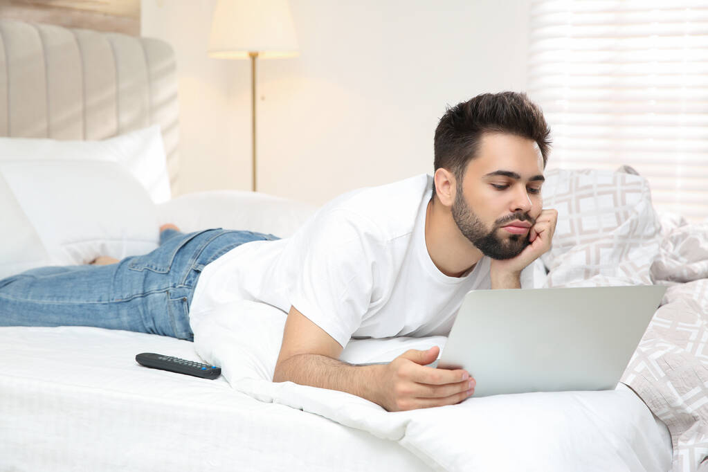 Fauler junger Mann mit Laptop zu Hause im Bett - Foto, Bild