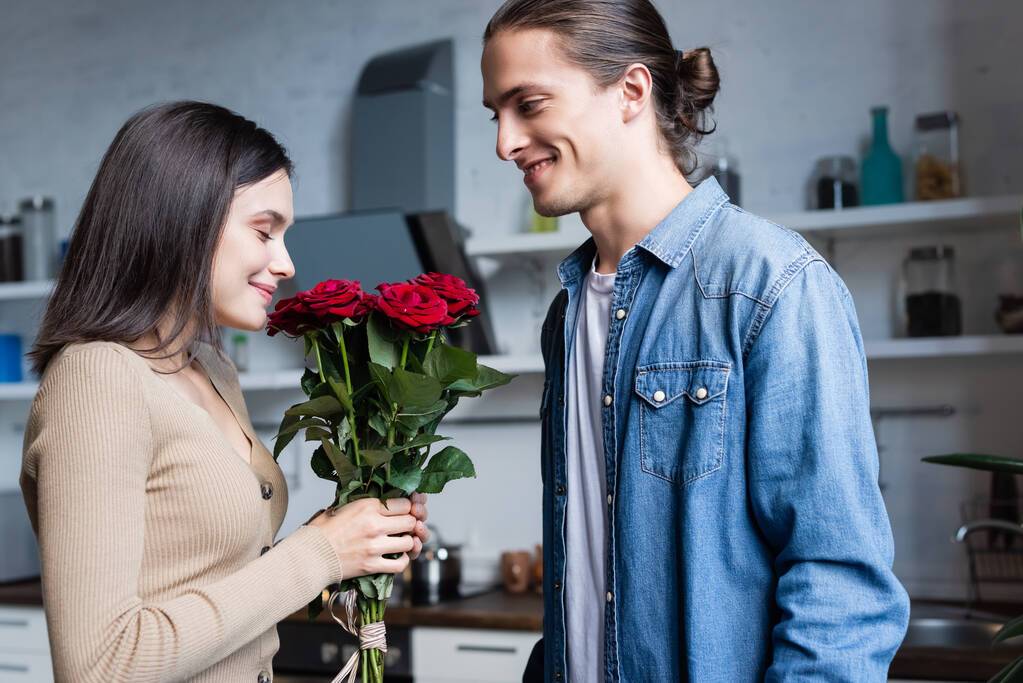 heureux femme tenant bouquet de roses avec les yeux fermés près du jeune homme - Photo, image