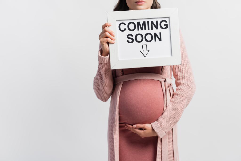 Ausgeschnittene Ansicht einer schwangeren Frau Haltetafel mit bald erscheinendem Schriftzug isoliert auf Weiß - Foto, Bild