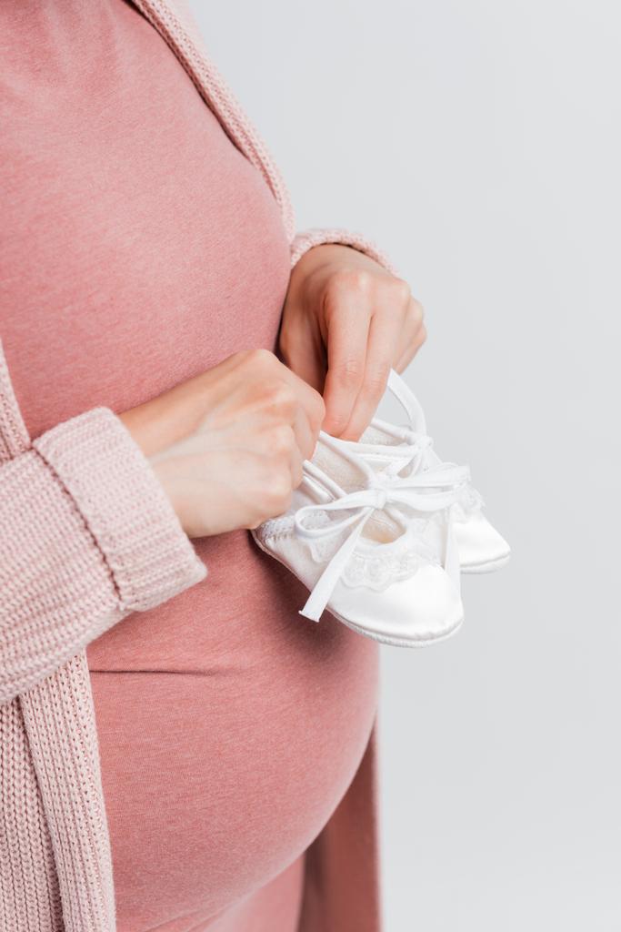 bijgesneden weergave van zwangere vrouw met kleine baby laarzen geïsoleerd op wit - Foto, afbeelding