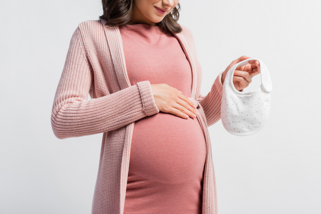 abgeschnittene Ansicht einer schwangeren Frau mit kleinem Baby-Lätzchen auf weißem Grund - Foto, Bild