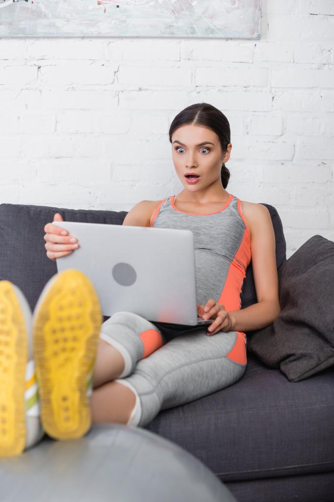 szelektív fókusz sokkos és terhes nő nézi laptop a nappaliban - Fotó, kép