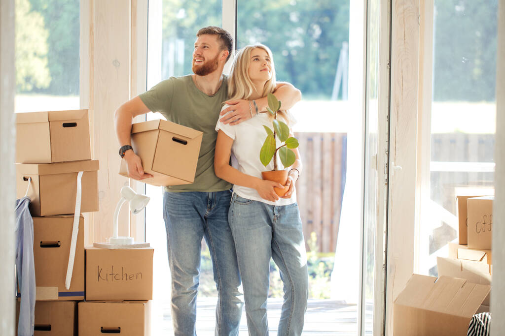 Felice coppia che trasporta scatole di cartone in una nuova casa il giorno del trasloco - Foto, immagini