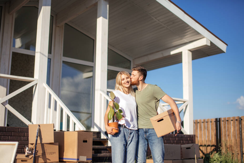 Муж и жена стоят перед новой покупкой дома с коробками - Фото, изображение