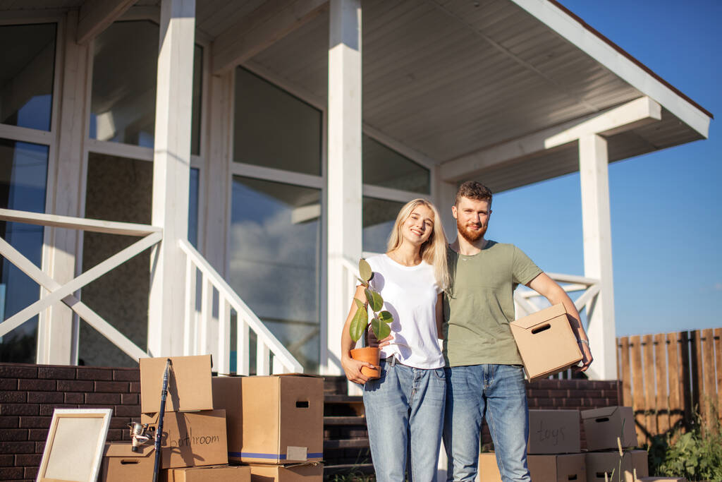 Husband and wife standing in front of new buying home with boxes - Photo, Image