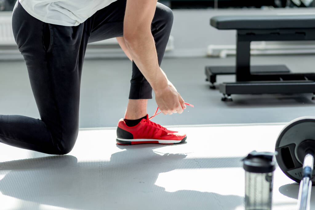 Knappe blanke sportman bindt zijn rode sneakers in de fitness studio - Foto, afbeelding