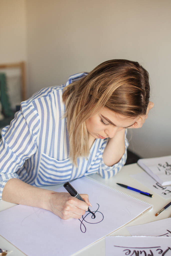 Женщина делает каллиграфические надписи, рисует на бумаге кистью для вывески - Фото, изображение