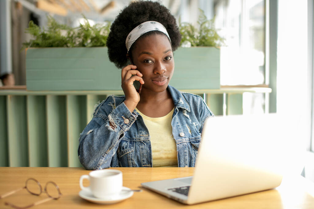 Mujer africana joven con pelo oscuro muy rizado de compras en línea mientras está sentado en la cafetería. - Foto, Imagen