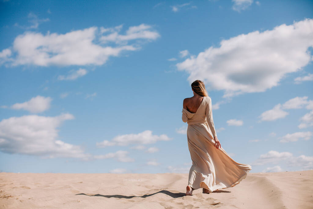 Молода струнка дівчина в бежевому платті ходить в пустелі
 - Фото, зображення