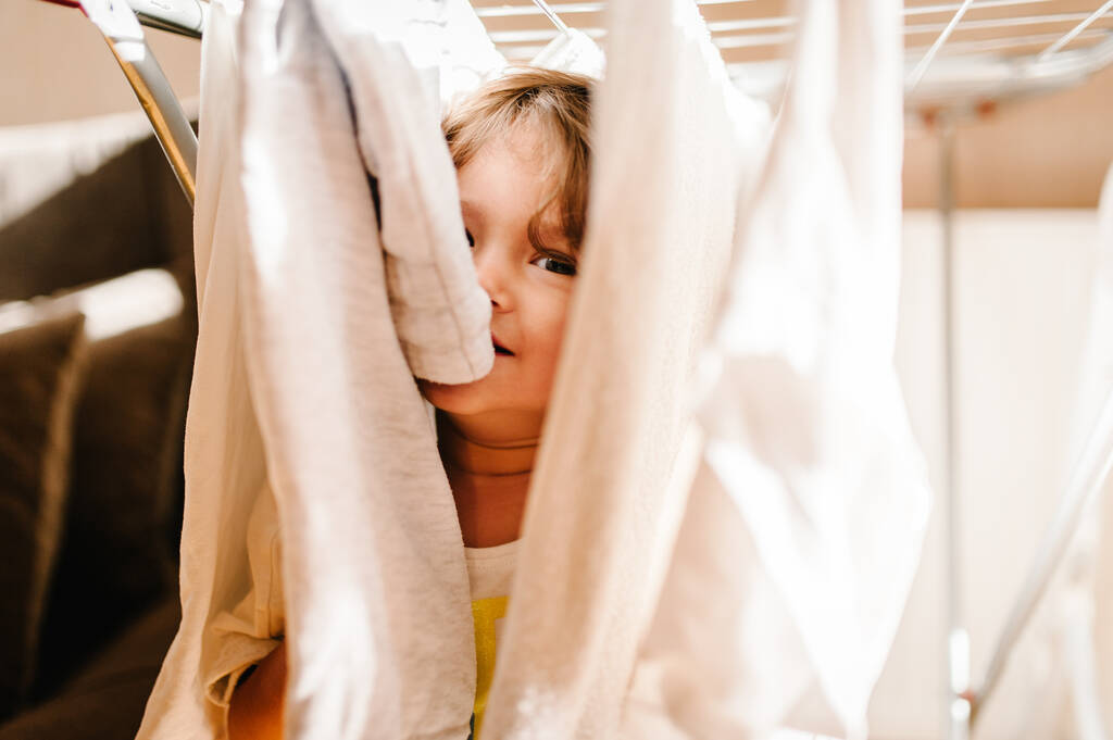 Porträt eines kleinen, hübschen, niedlichen Kleinkindes, Mädchens, entzückenden Babys, das Wäsche an der Wäscheleine hängt und zu Hause auf dem Boden spielt. - Foto, Bild