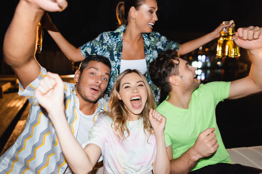 Επιλεκτική εστίαση των ενθουσιασμένων φίλων με μπύρα κατά τη διάρκεια του πάρτι σε εξωτερικούς χώρους τη νύχτα  - Φωτογραφία, εικόνα