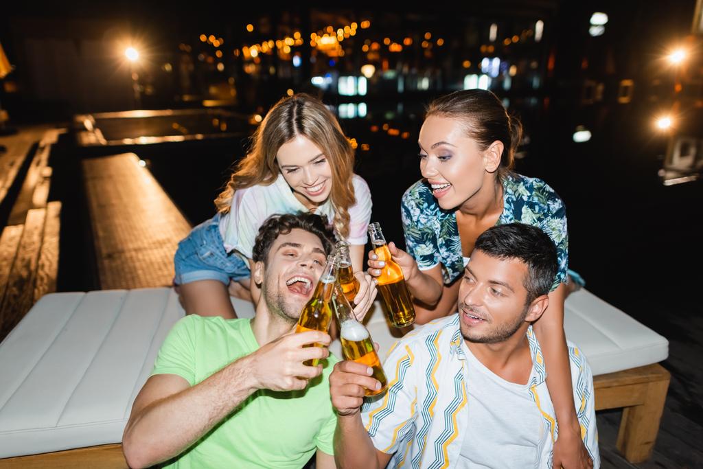 Νεαροί φίλοι κάνουν πρόποση με μπουκάλια μπύρας κοντά στην πισίνα τη νύχτα  - Φωτογραφία, εικόνα