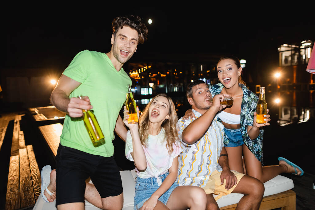 Enfoque selectivo de amigos que beben cerveza al aire libre por la noche  - Foto, Imagen