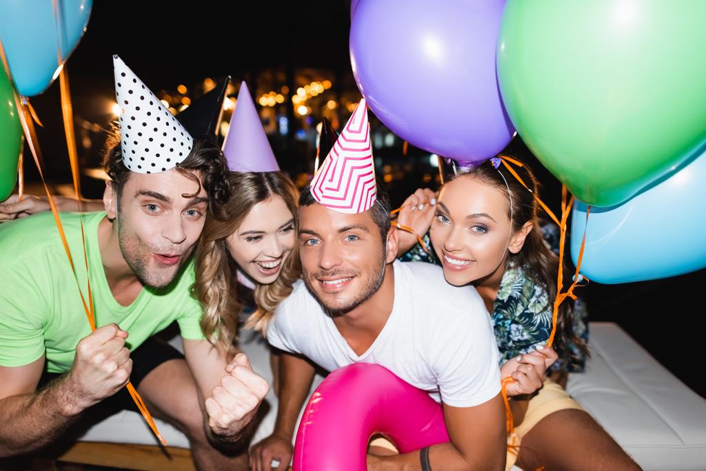 Молодые друзья смотрят в камеру во время вечеринки с воздушными шарами ночью  - Фото, изображение
