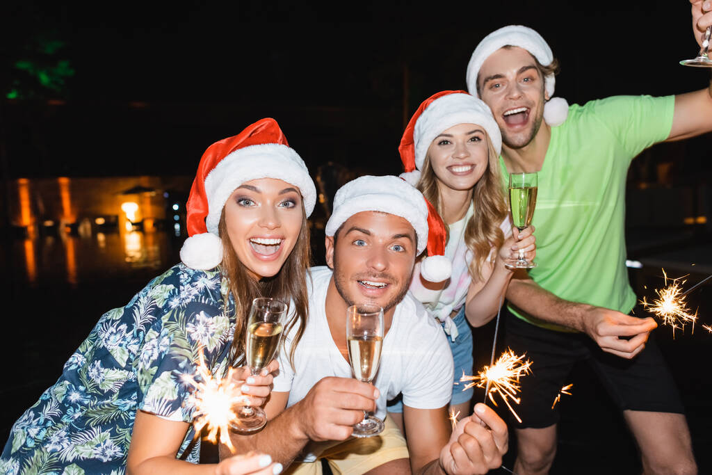 Foco seletivo de jovens que celebram o Ano Novo com champanhe e faíscas à noite ao ar livre  - Foto, Imagem