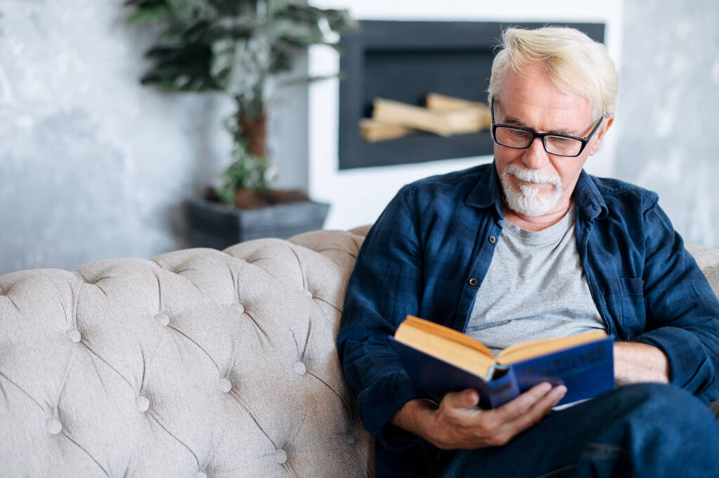 A szemüveges felnőtt férfi könyvet olvas. - Fotó, kép