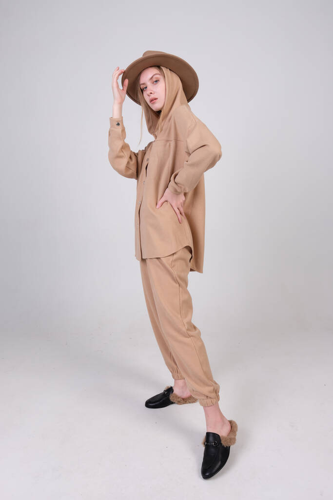 Modemodel in lässigem beigen Anzug und Hut posiert im Studio für Look Buch und Kleidungskatalog. - Foto, Bild