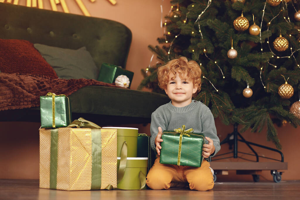 Kisfiú a karácsonyfa közelében, szürke pulcsiban. - Fotó, kép