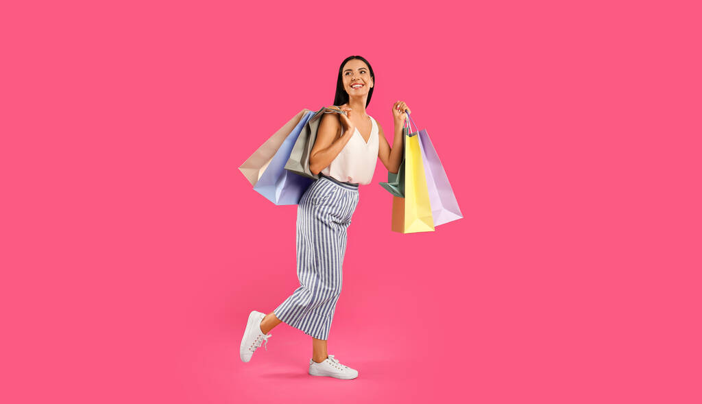 Schöne junge Frau mit Papiereinkaufstaschen auf rosa Hintergrund - Foto, Bild