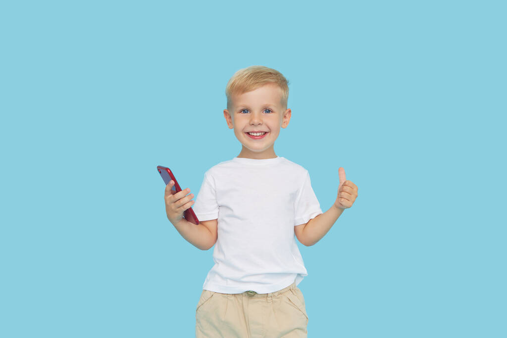 Mavi arka planda akıllı telefonu olan sevimli, gülümseyen çocuk. Çocuklar için cep telefonuyla eğitim uygulamalarının reklamını yapmak. Komik surat..  - Fotoğraf, Görsel
