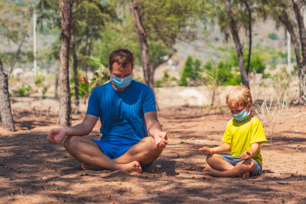 Sport kinderen. Vader mediteert yoga poseren nauwe ogen in bospark lucht, zoon herhaalt, imiteren gedrag, dragen gezicht blauw masker beschermen coronavirus lopen natuur zon dag. Papa invloed op jongen wereldbeeld - Foto, afbeelding