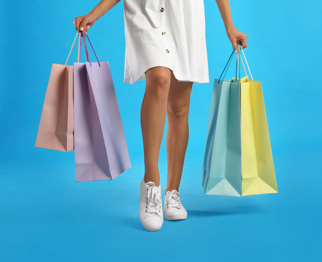 Mujer joven con bolsas de compras de papel sobre fondo azul claro, primer plano - Foto, Imagen