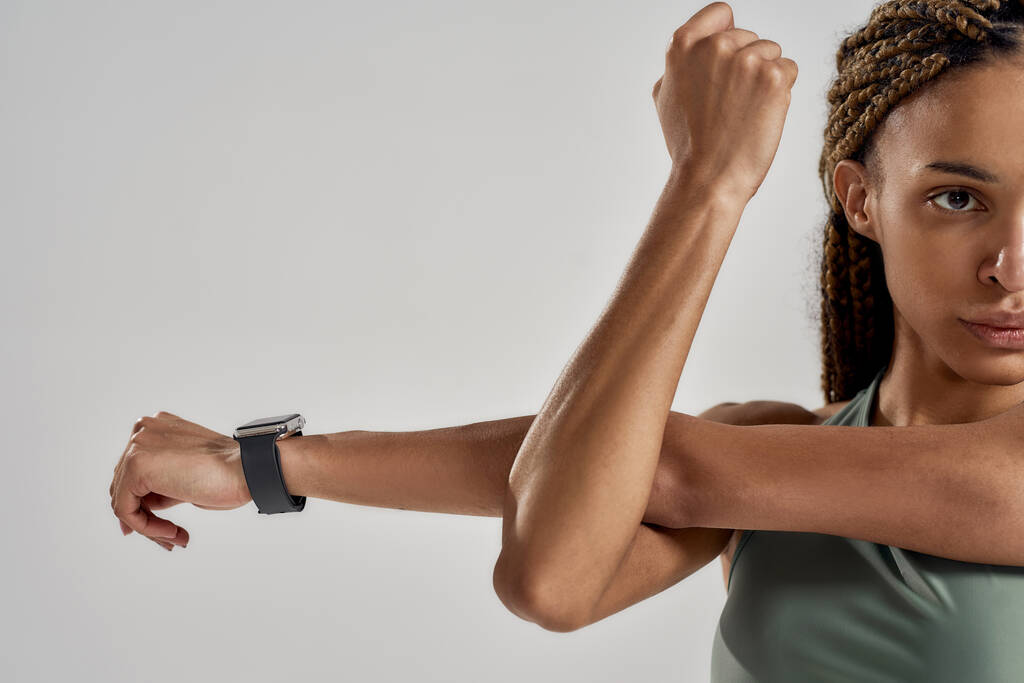 Nahaufnahme einer jungen Mixed Race Fitness Frau im Sportdress, die ihre Arme vor dem Training ausstreckt, während sie isoliert vor grauem Hintergrund steht - Foto, Bild