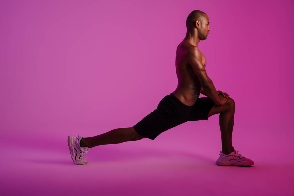 Kuva komea keskittynyt afrikkalainen kunto urheilu mies eristetty vaaleanpunainen seinä tausta tehdä venyttely harjoituksia - Valokuva, kuva