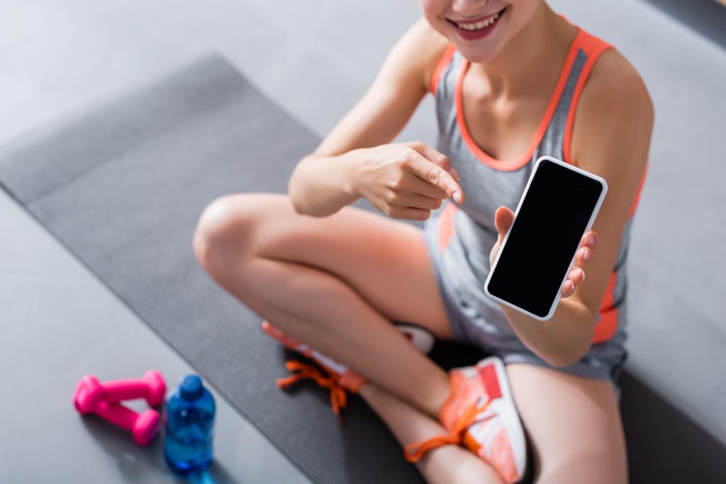 Spor kıyafetli bir kadının spor kıyafetli görüntüsü spor minderinde boş ekranlı akıllı telefonu işaret ediyor.  - Fotoğraf, Görsel