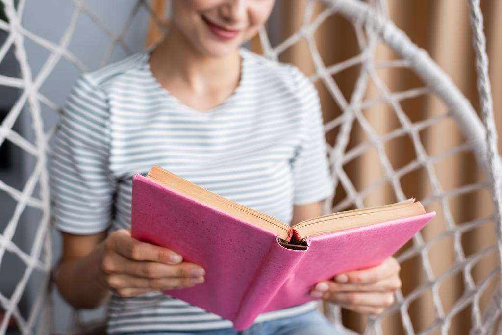 Oříznutý pohled na mladou ženu čtení knihy v závěsné křeslo doma  - Fotografie, Obrázek